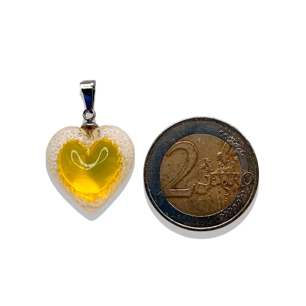 Pendentif cœur Voronoï jaune en résine présenté à côté d’une pièce de 2 euros pour montrer la taille du bijou