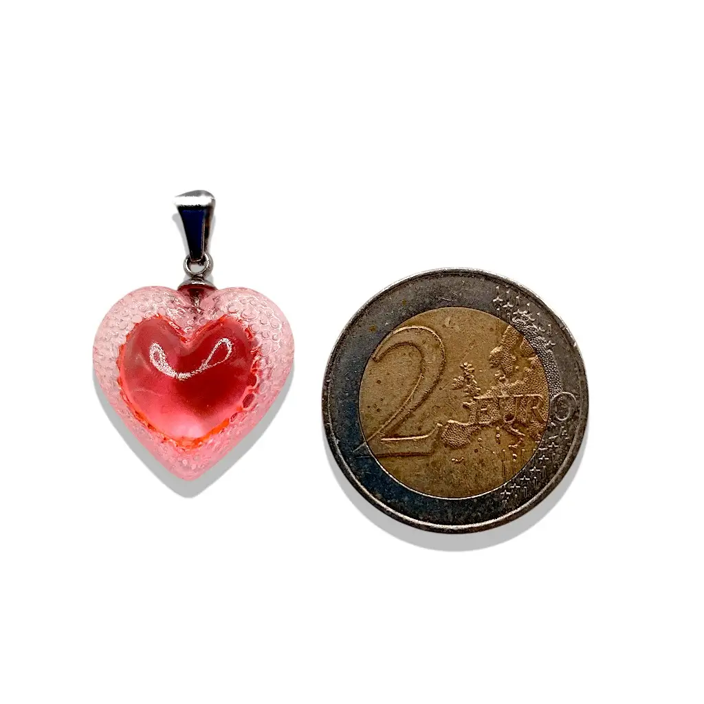 Pendentif cœur Voronoï rose en résine présenté à côté d’une pièce de 2 euros pour montrer la taille du bijou