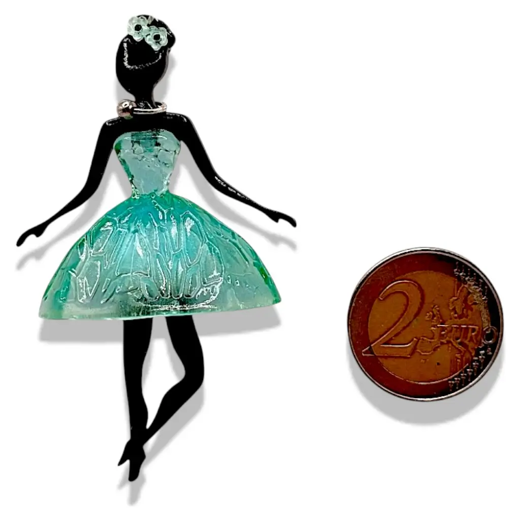 Pendentif Pépette bleue/verte en résine placé à côté d’un objet de référence pour montrer les dimensions