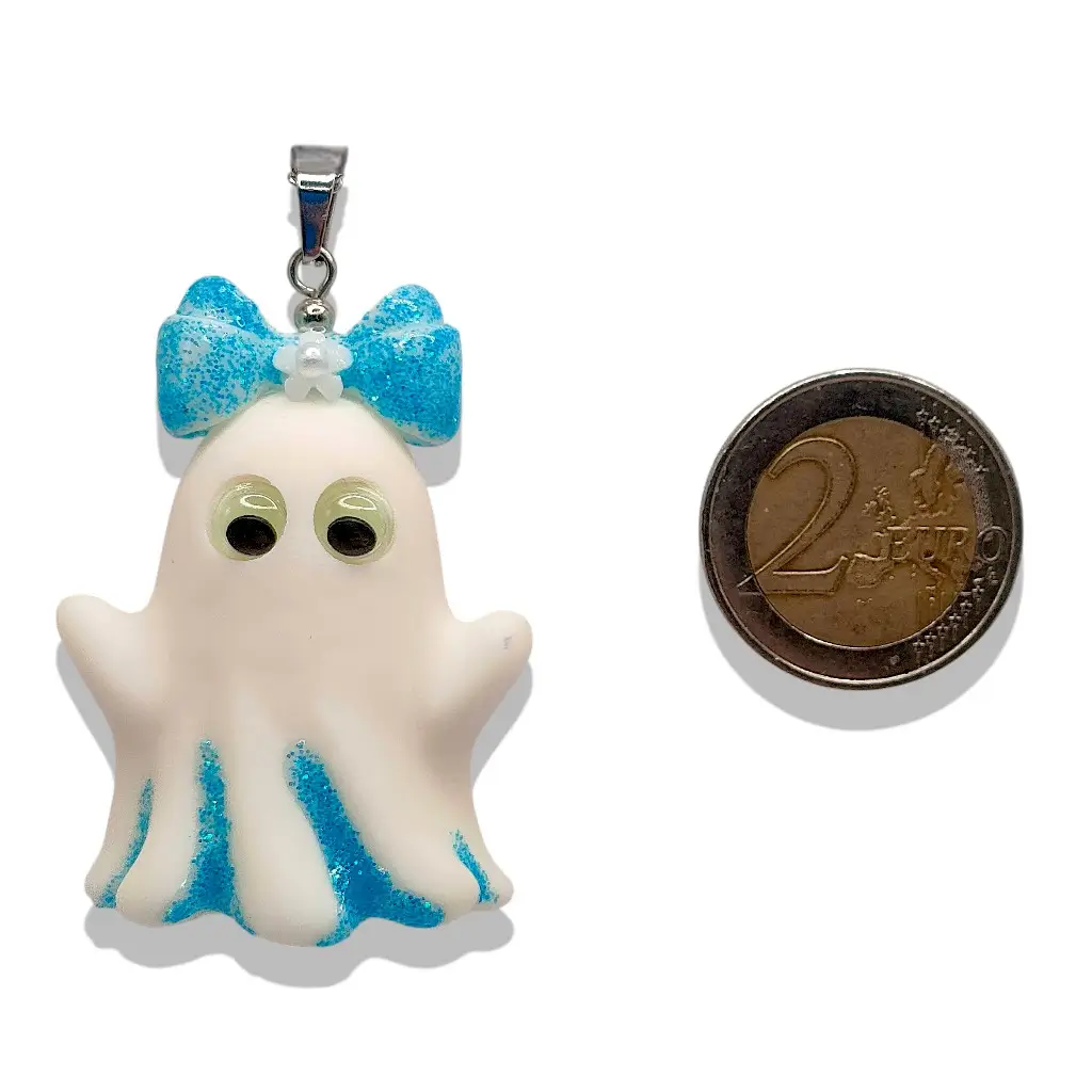Pendentif Fantômette bleue en résine avec paillettes et yeux phosphorescents à côté d’une pièce de 2 € pour référence taille