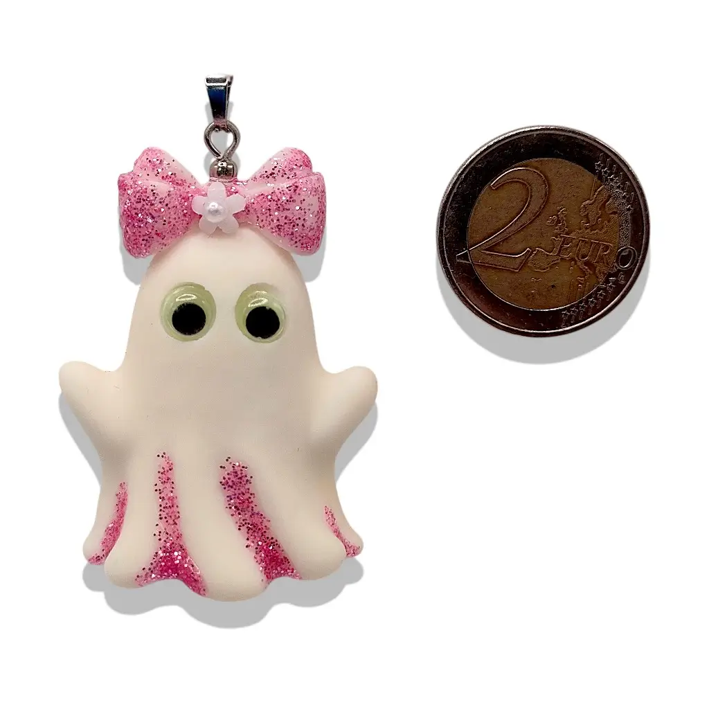 Pendentif Fantômette rose en résine avec paillettes et yeux phosphorescents à côté d’une pièce de 2 € pour référence taille