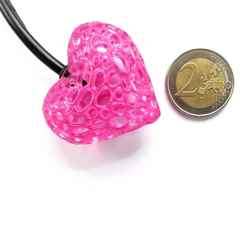 Collier cœur alvéolé rose présenté à côté d’une pièce de 2 euros pour comparer les dimensions